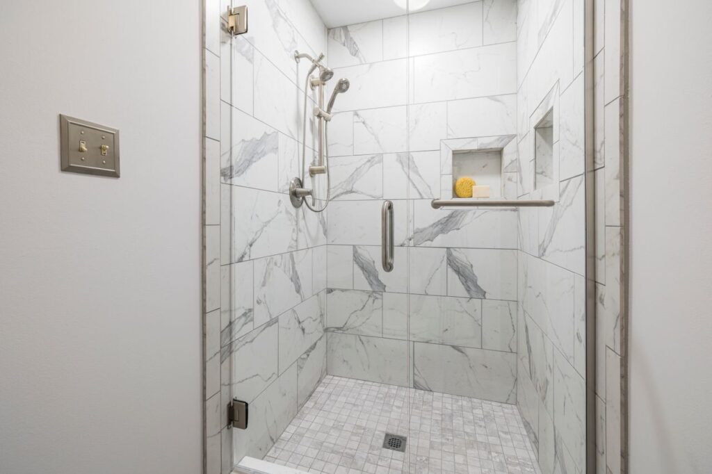 Elegant bathroom with white marble tiles and glass door, showcasing modern interior design.